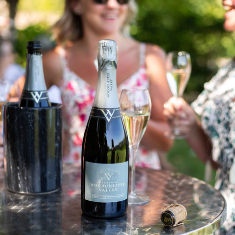 Sparkling wine bottle with Woodchester Valley label and cork, on table with glasses
