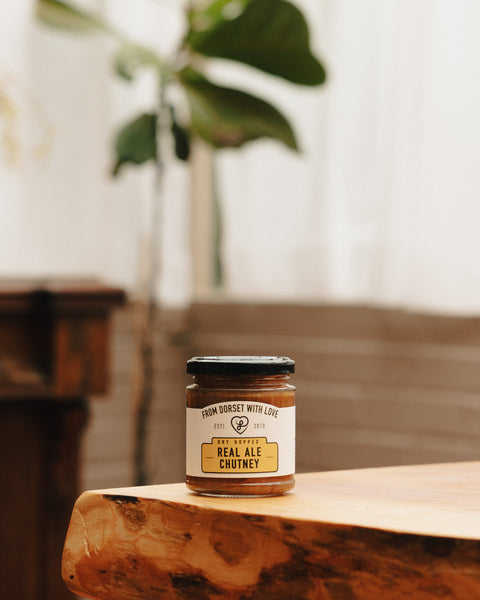 Small glass chutney jar on wooden surface with amber contents and printed label