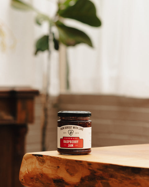 Raspberry jam jar with red jam and label on wooden surface