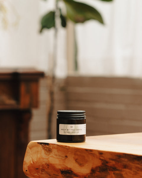 Small black glass candle jar with “Held by the Earth” label