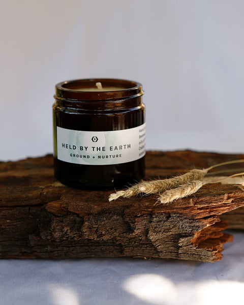 Black glass candle jar with cream wax and “Held by the Earth” label
