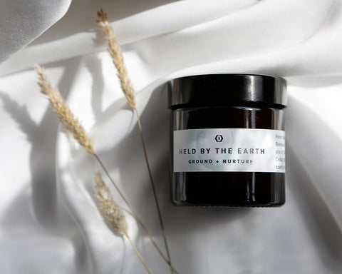 Black glass candle jar with metal lid, “Held by the Earth” label visible