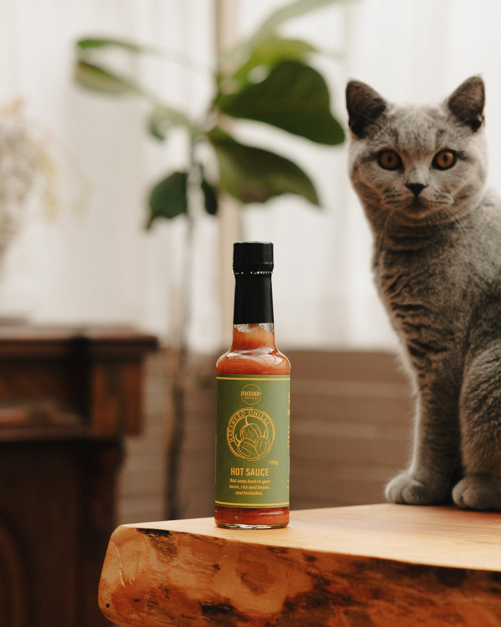 Small habanero hot sauce bottle with orange liquid and green label on wood