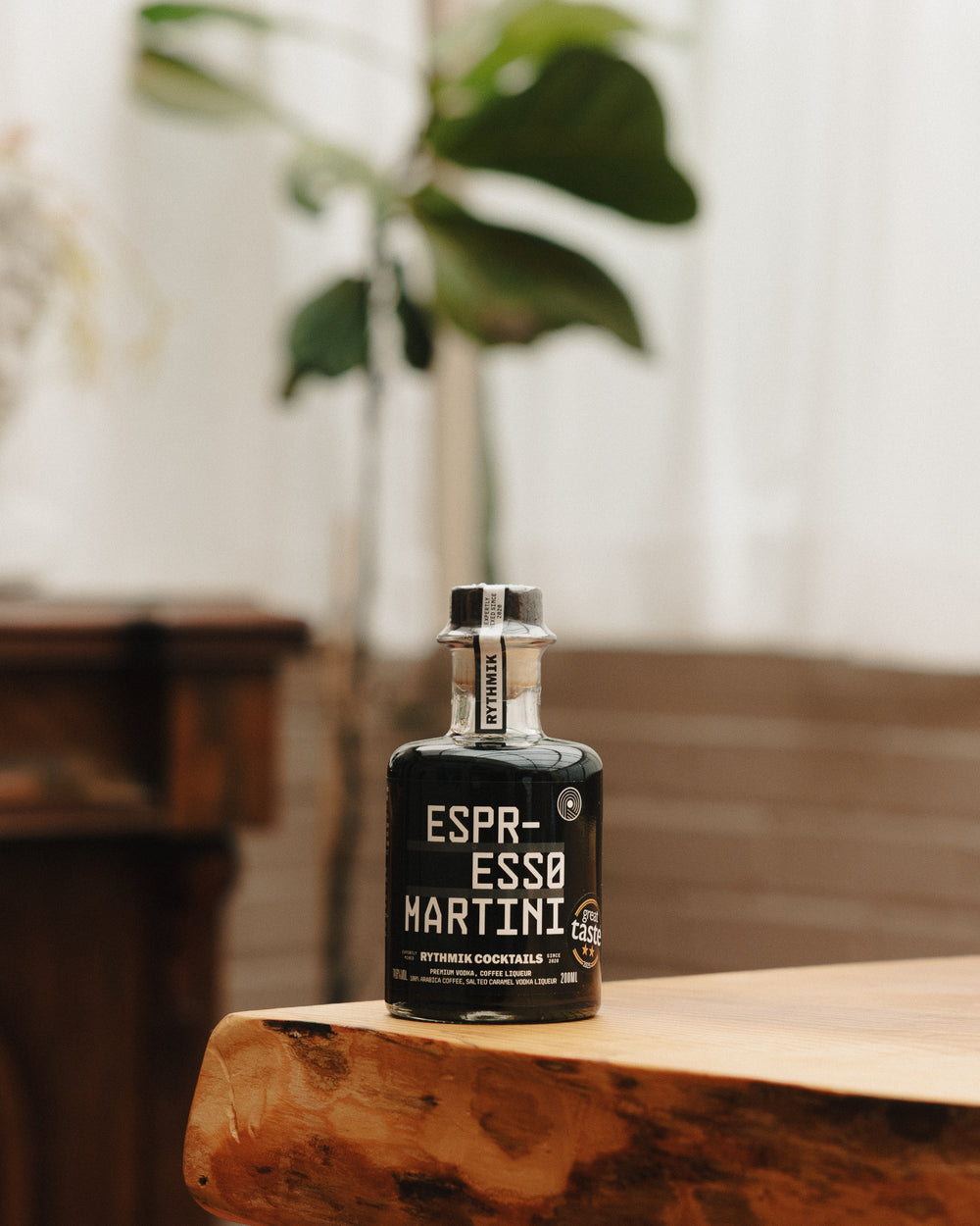Espresso martini liqueur bottle standing on a wooden tabletop with blurred indoor plants
