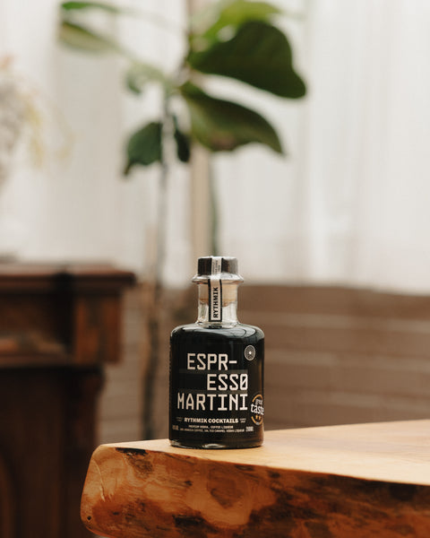 Espresso martini liqueur bottle standing on a wooden tabletop with blurred indoor plants
