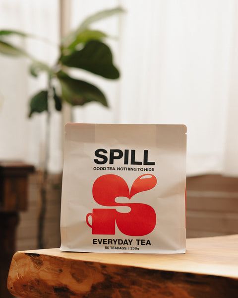 SPILL Everyday Tea pouch on wooden table, white with orange logo