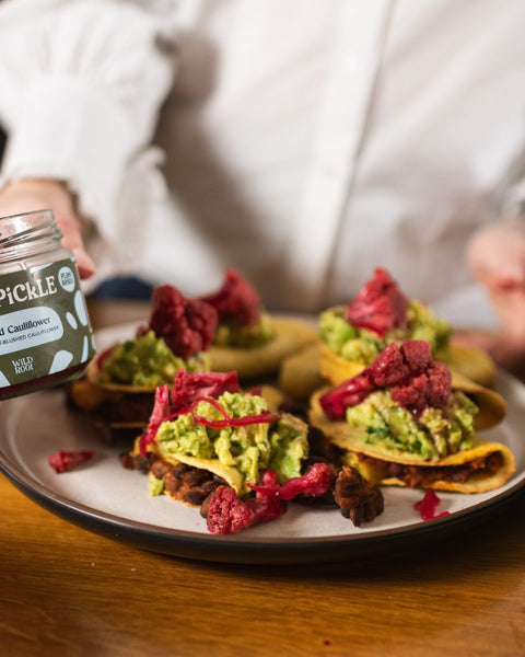 Tacos topped with pink pickled cauliflower, with a Wild Root jar partly visible beside the plate.