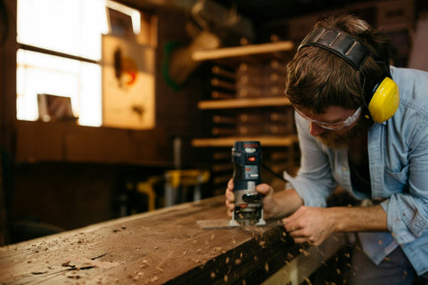 Man using a power drill in a workshop with tools and equipment in the background.
