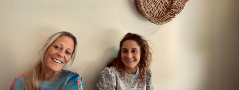 Two women sitting together with a decorative woven basket in the background.