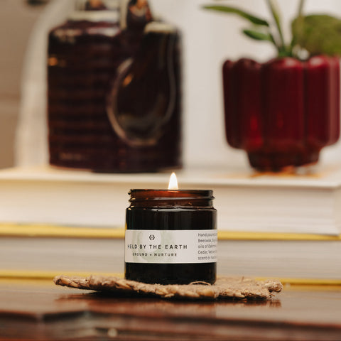 Candle labeled ' Held by the Earth' on a wooden surface with a blurred background