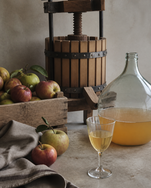 AI-assisted editorial still life of apples, a wooden press and cider vessels.